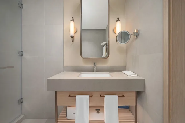 Elegantna svijetla kupaonica s velikim ogledalom, toplim osvjetljenjem i prirodnim materijalima.