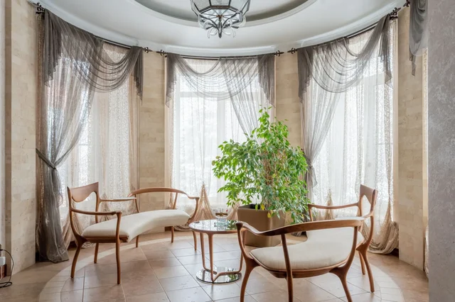 Elegantna dnevna soba s velikim prozorom i mekanim zavjesama od prirodnih materijala, uz puno prirodnog svjetla.